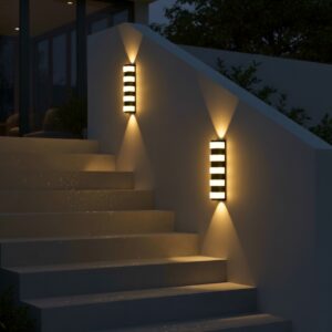 Modern black outdoor LED wall light, 12W, glowing warm up and down on a luxury home's grey exterior staircase at night.