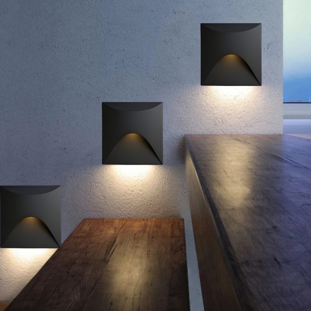 A modern, black, square-shaped step light with a curved, flowing front design