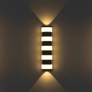 Modern black outdoor LED wall light, 12W, glowing warm up and down on a luxury home's grey exterior staircase at night.