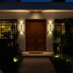 Modern black outdoor LED wall light, 12W, glowing warm up and down on a luxury home's exterior at night.